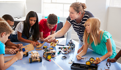 An adult and a group of students gathered around robotics elements on a table